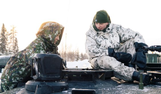 Two conscripts on top of a tank on a sunny winter day. The conscript on the left is wearing a cold weather jacket, model m05. The one on the right is wearing a snow camouflage suit.