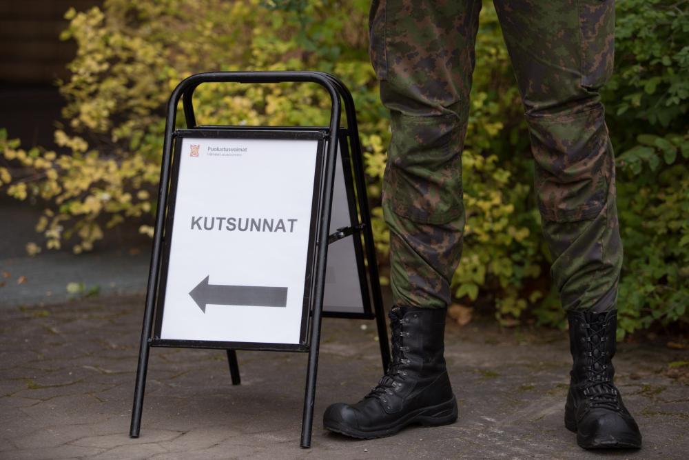 Kutsuntoihin ohjaava kyltti, jonka vieressä seisoo sotilas.