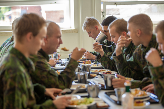 Varusmiehiä maastopuvussa ruokailemassa pitkän pöydän äärellä