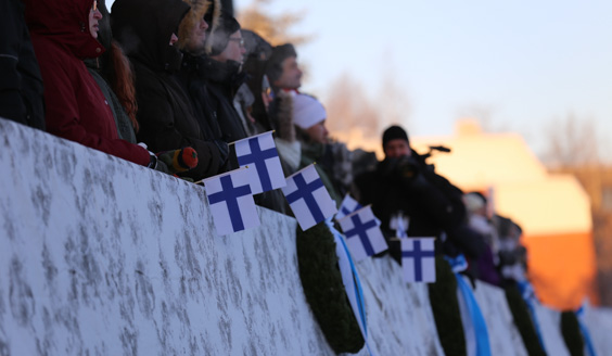 Kaidetta vasten ihmisiä joilla on käsissään pieniä Suomen lippuja