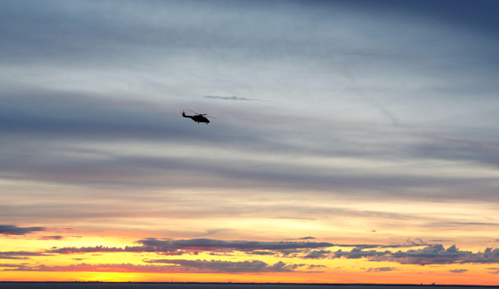 Kuvituskuva. Auringonlaskussa lentää kaukana Puolustusvoimien NH90-kuljetushelikopteri.