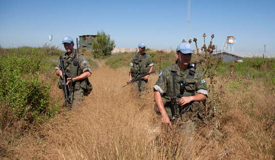 Kolme suomalaista sotilasta heinikossa siniset lippalakit päässä