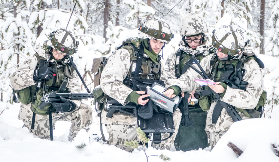 Talvisessa lumisessa kuvassa neljä taistelijaa polviasennossa tarkastelemassa johtajan johdolla tilannetta ja valmistautumassa jatkamaan tehtävää.