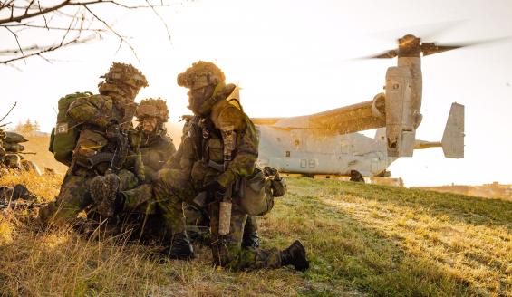Three soldiers squatting in a field and an airplane in the background