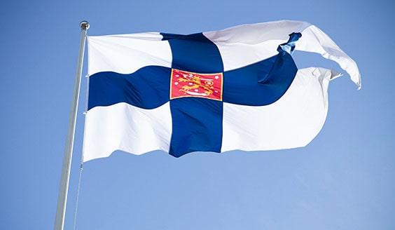 Suomen kielekkeinen valtiolippu sinistä taivasta vasten. 