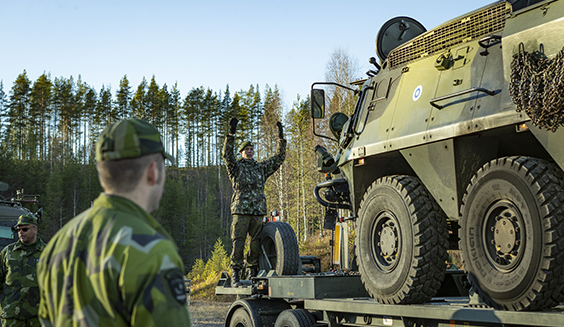 Soldier is giving driving instructions with his hands to a soldier driving an armored vehicle