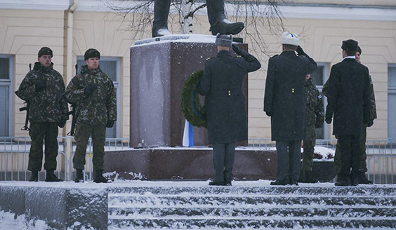 Neljä sotilasta muistomerkin sivuilla rynnäkkökiväärien kanssa. Upseerit tervehtivät muistomerkkiä sen edessä.