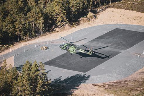 an NH-90 helicopter landing on an asphalted refuelling site, a large field with its protection areas. Forest in the background