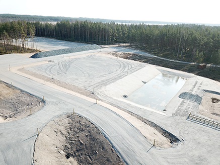 Syndalenin uuden räjäytyspaikan aukea, laaja alue, jossa on Syndalenin uuden räjäytyspaikan räjäytyskenttä, vedenkäsittelyallas, sekä kivimurskeesta tehty suojamuuri. Takana metsää.