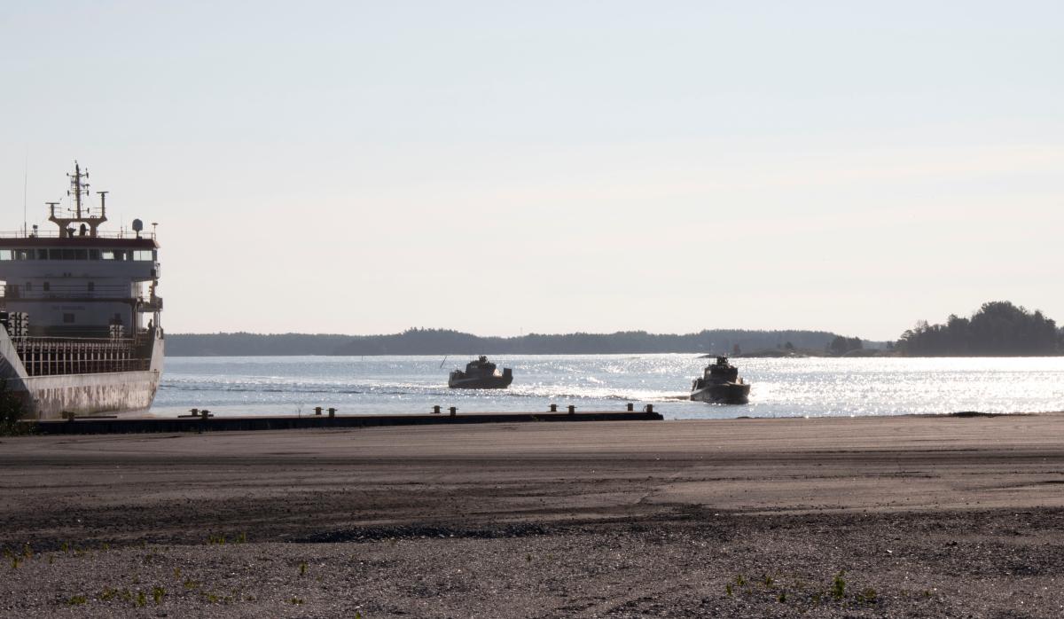 Kaksi sotilasalusta saapumassa satamaan, vasemmassa laidassa satamassa siviilirahtialus.