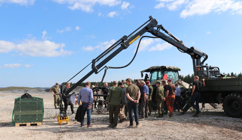 Joukko ihmisiä katselee traktoriin kiinnitettyä laitetta.
