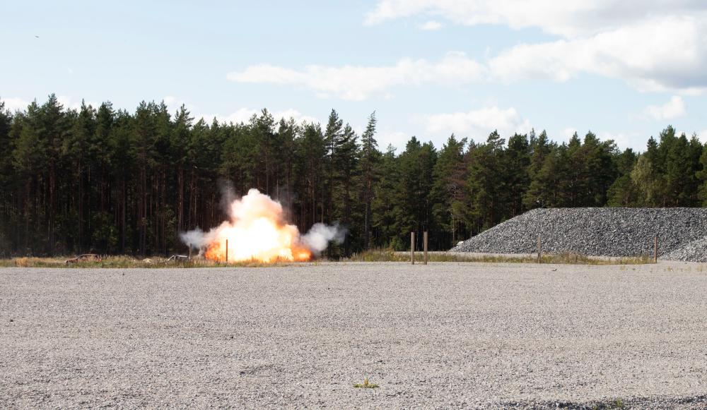 Hiekkakentän perällä iso räjähdys tulipallo, taustalla metsää.