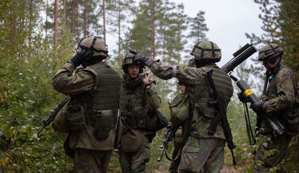 Viiden sotilaan joukko metsässä, johtaja osoittaa sormella vasemmalle.