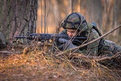 Urheilukoulun varusmies tähtää rynnäkkökivääri kädessään maastossa.