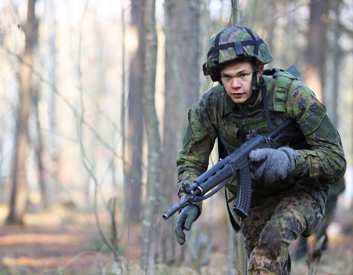 Varusmies taisteluvarustuksessa juoksemassa metsässä.