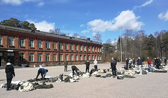 Alokkaat siviilivaatteissa varustesäkkien sisältöä tarkastamassa komppanian edessä