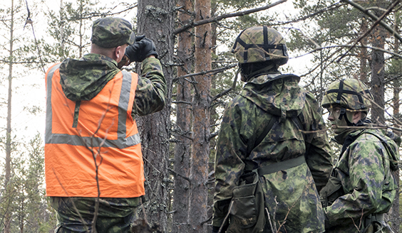 Sotilaat seuraavat vierestä kun oranssiliivinen kouluttaja opettaa heitä