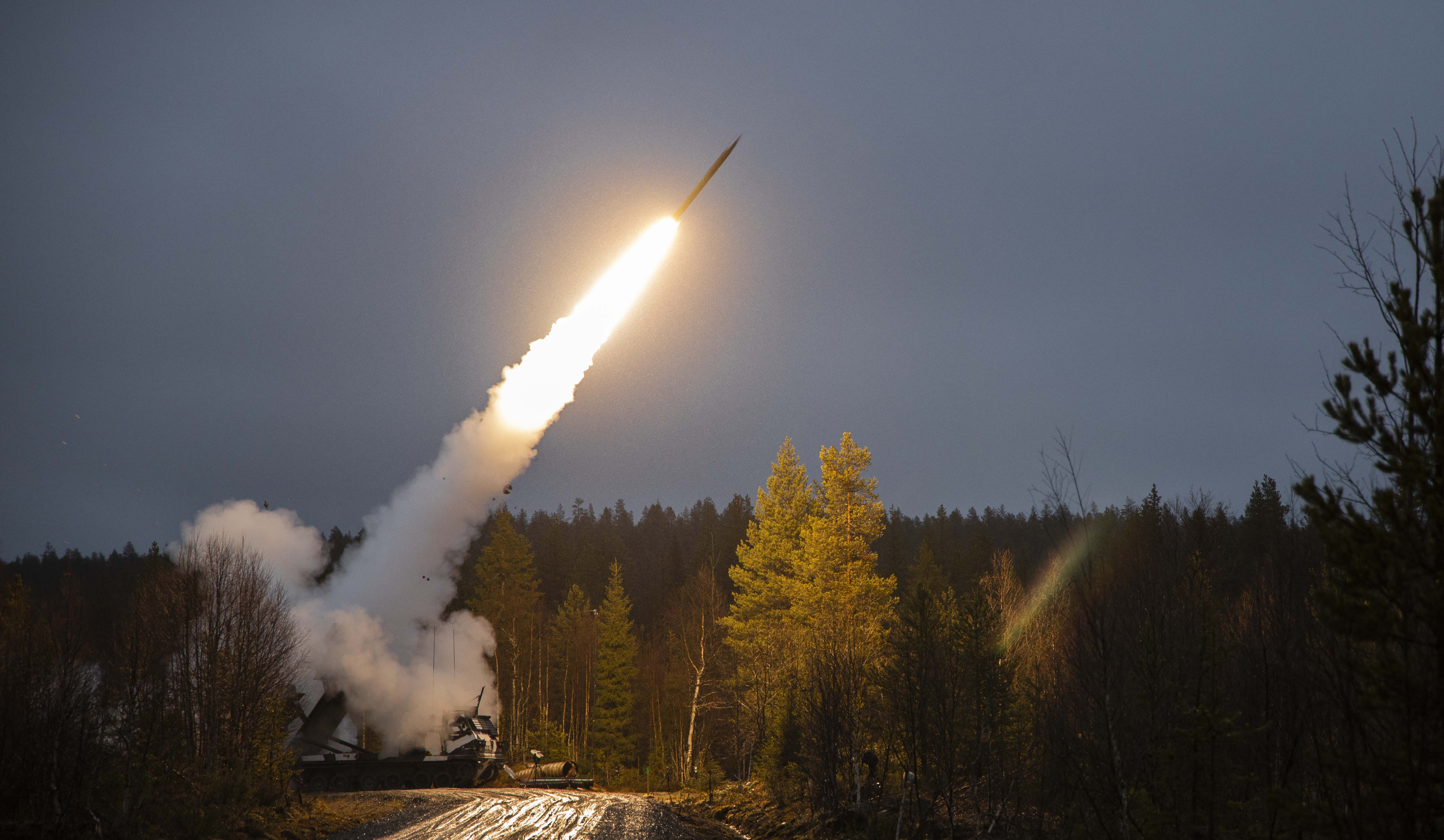 Kuva jossa raskas raketinheitin on tiellä ja ampuu raketin ilmaan.