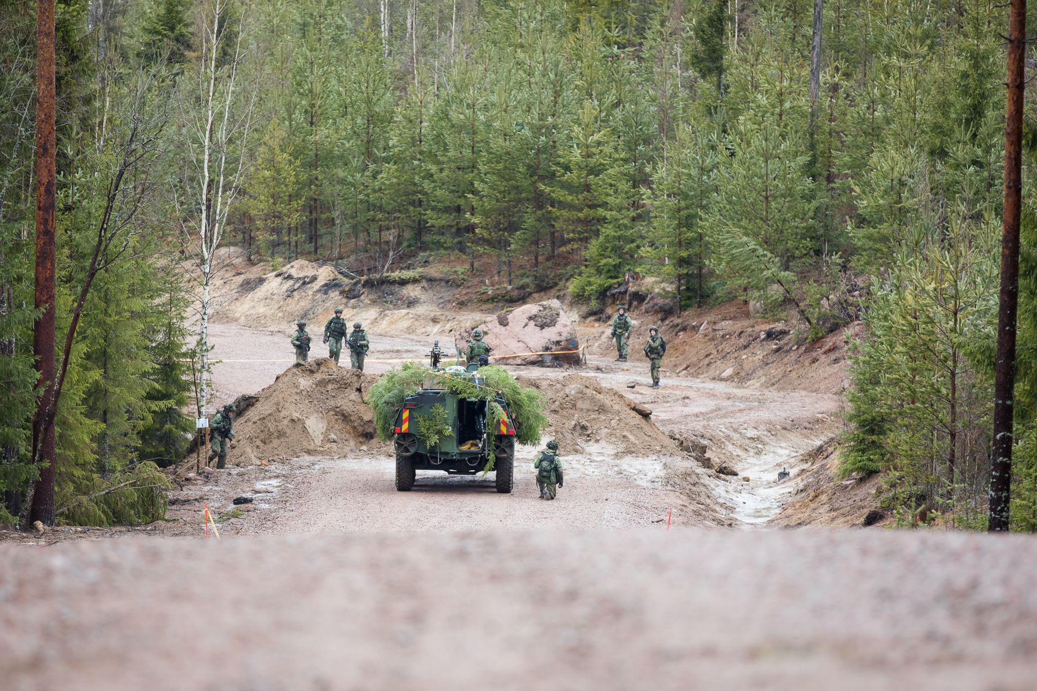 Pioneereja tiellä, esteenä etenemiselle iso hiekkakasa. Kulkuneuvo on maastoutettu havuilla.