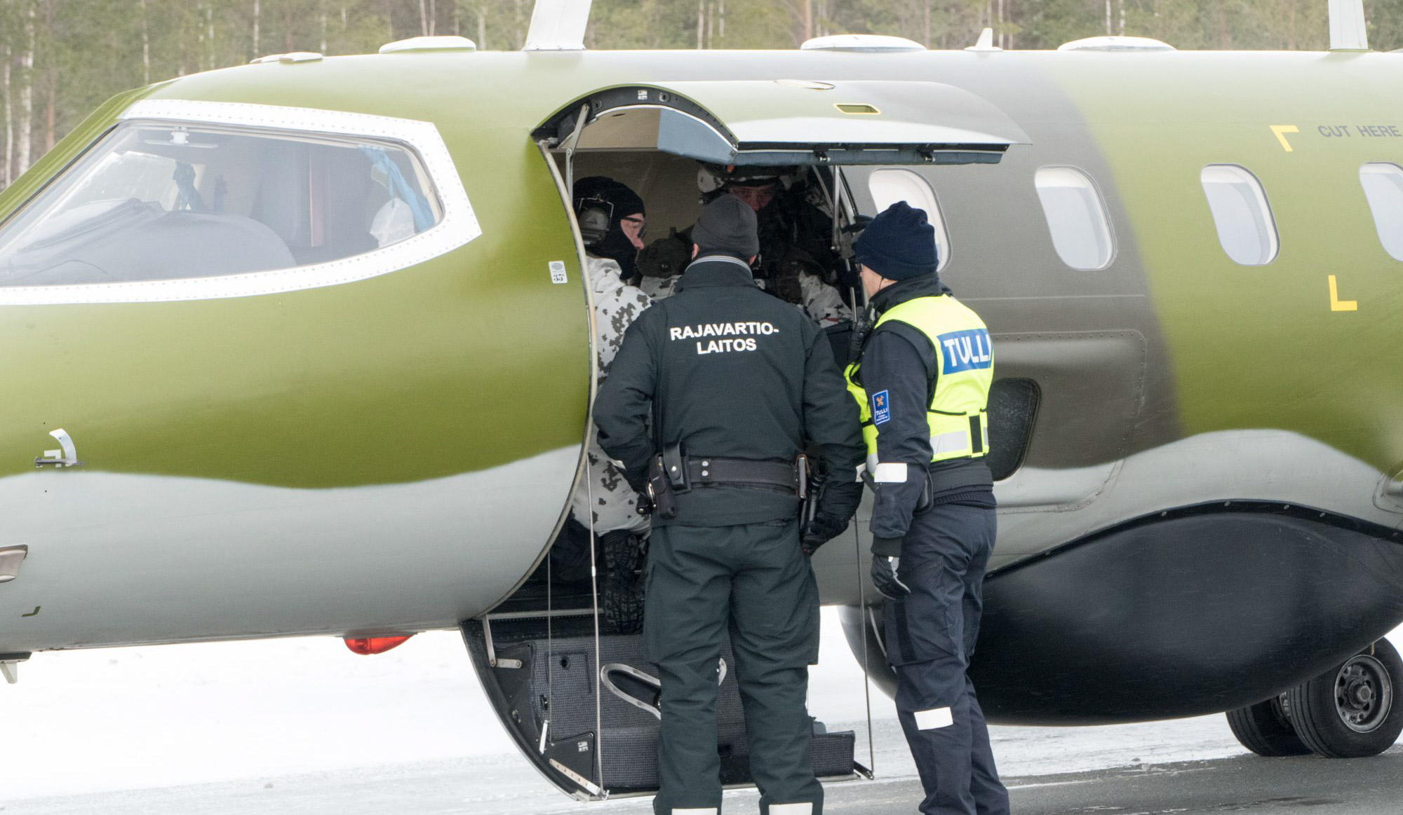 Lentokone jonka sisällä on sotilaita. Ovella kaksi henkilä joista toisella lukee selässä "Rajavartiolaitos" ja toisella "Tulli".