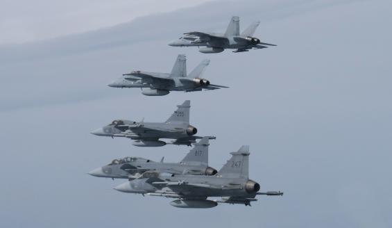 Two Finnish F/A-18 Hornet fighter jets and three Swedish Gripen fighter jets fly in formation above clouds