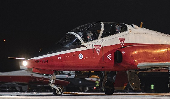 Punavalkoinen Hawk-suihkuharjoituskone maassa pimeään vuorokaudenaikaan valot sytytettynä.