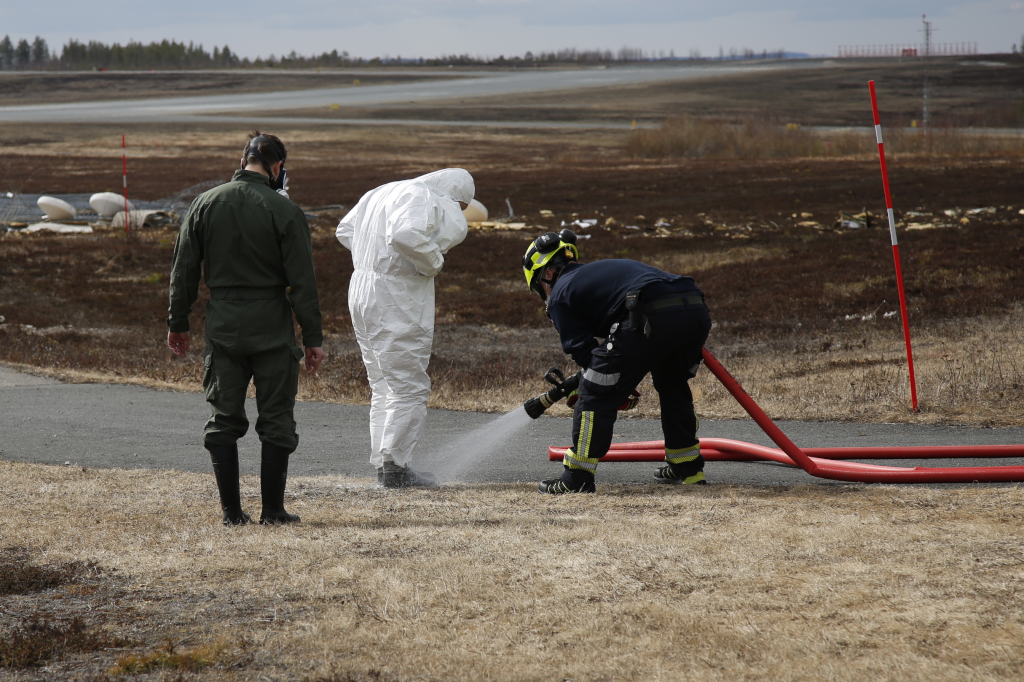 Kolme henkilöä suojavarusteissa, taustalla näkyy lentokenttäaluetta.