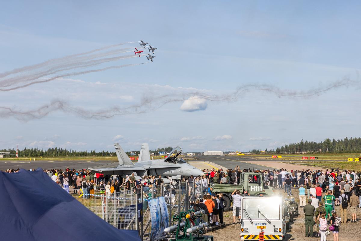 Yleisöä maassa olevan Hornet-hävittäjän ympärillä, taivaalla lentää Midnight Hawks -taitolentoryhmä Hawk-hävittäjillä tiiviissä nipussa.