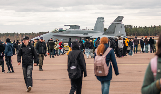 Yleisnäkymä lentokentän alueella vaeltavista ihmisistä. Taustalla Hornet -hävittäjä.