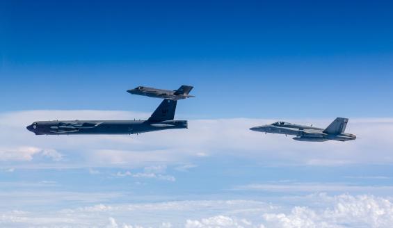 Ilmassa otetussa kuvassa yhdysvaltalainen B-52-pommikone lentää kirkkaan sinisellä taivaalla alapuolellaan tiivis pilvipeite. Norjalainen F-35A ja suomalainen Hornet lentävät pommikoneen vierellä.