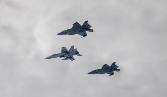 Suomen ilmavoimien Hornet-hävittäjä lentää pilvisellä taivaalla kahden Norjan kuninkaallisten ilmavoimien F-35A-hävittäjän kanssa.