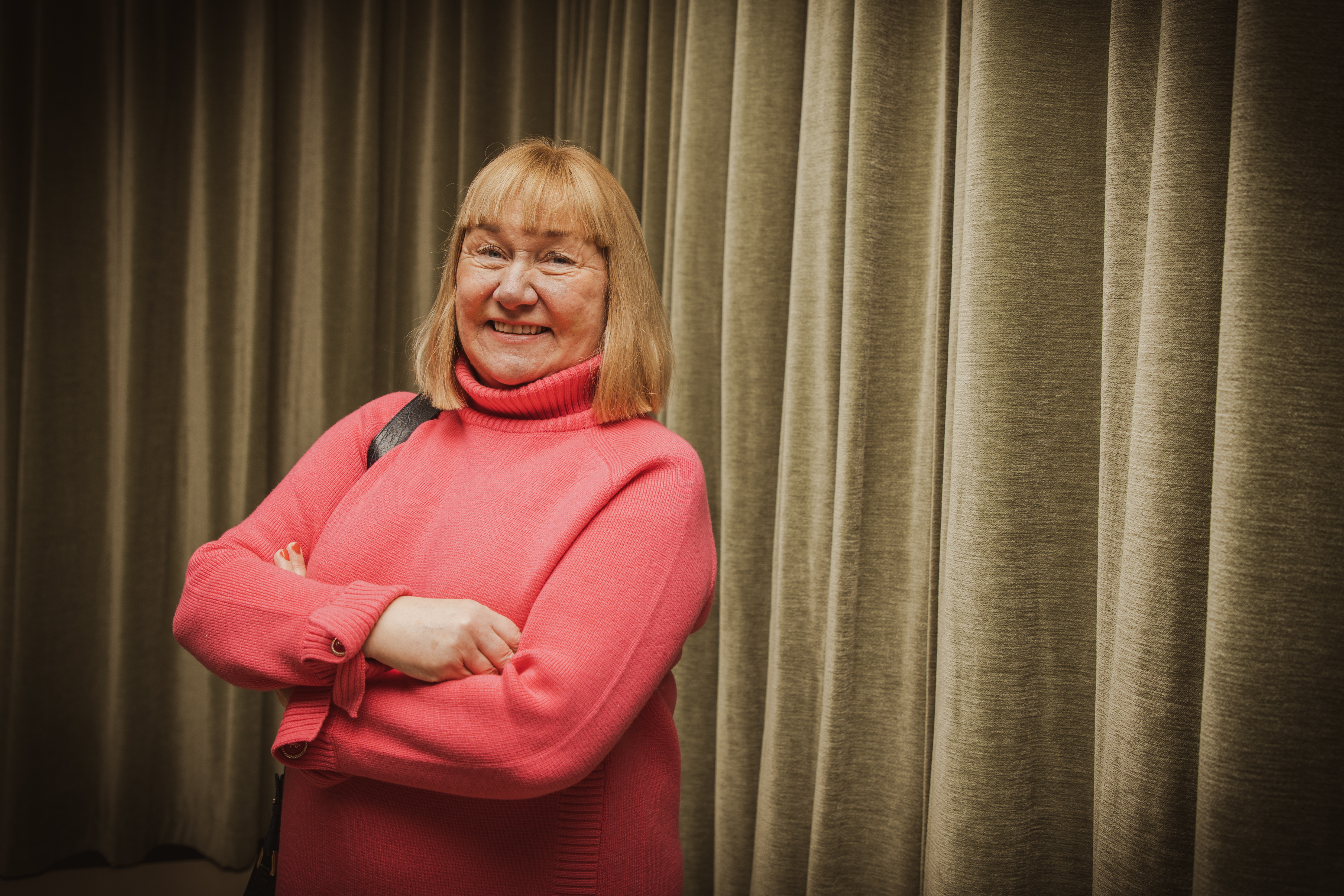 Kuvassa Hanna Snellman katsoo kameraan ja hymyilee vihreän verhon edessä. 