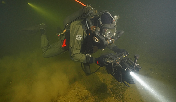 Raivaajasukeltaja tekee räjähde-etsintää vedenpinnan alapuolella sukellusvarusteissa.