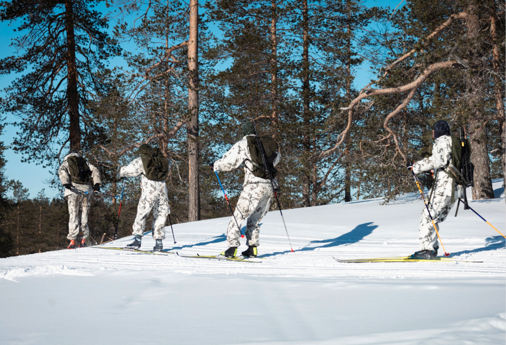 Kuvassa varusmiehet hiihtävät jonossa lumipuvut päällä.