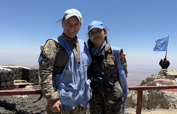Kaksi naista seisoo vierekkäin vuoren huipulla YK-varusteissa