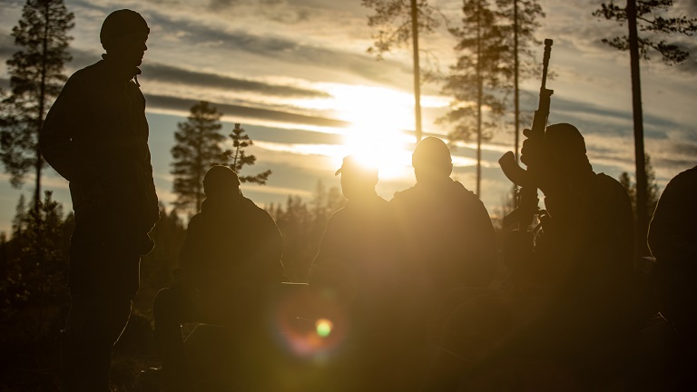 Kuvassa varusmiehiä auringonlaskussa metsässä. 