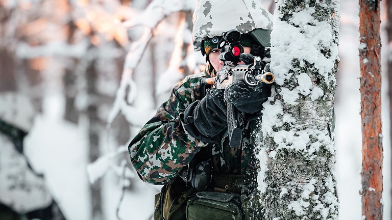 En soldat skjuter bakom ett träd i ett vinterlandskap.