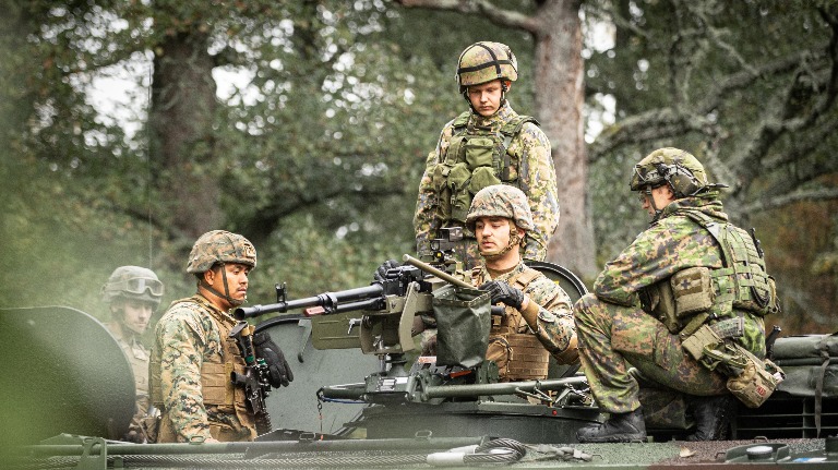 Finnish and American soldiers on top of an armored vehicle.