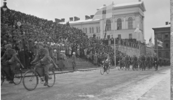Kuvassa on näkymä itsenäisyyspäivän paraatista Suurtorilta vuodelta 1940. Mustavalkoisessa kuvassa on sotilaita polkupyörien selässä. 