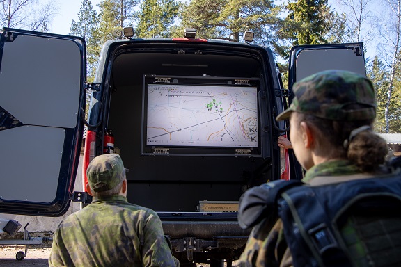 kuva jossa varusmiehet ja kouluttajat seuraavat auton perässä olevalta näytöltä, kuinka simulaattoreilla tuettu harjoitus on edennyt.