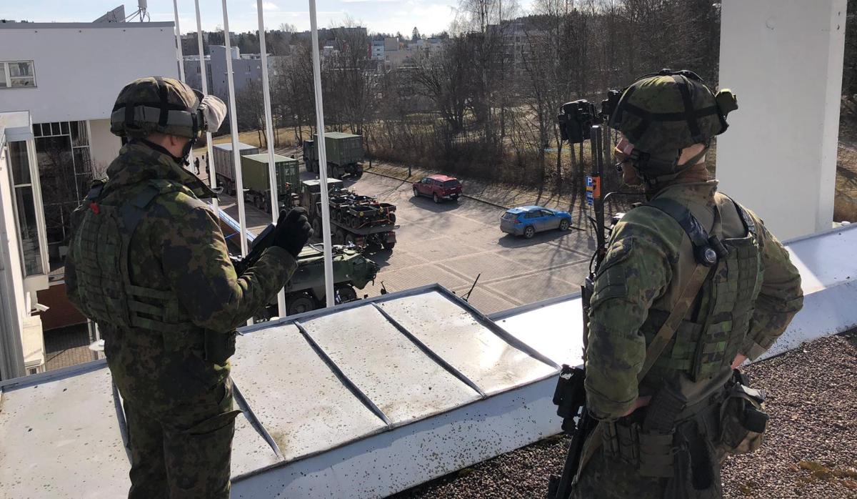 Kuvassa kaksi EUBG-osaston sotilasta talon katolla selin kameraan. Taustalla näkyy parkkipaikka, jossa osastoon kuuluvia sotilasajoneuvoja.
